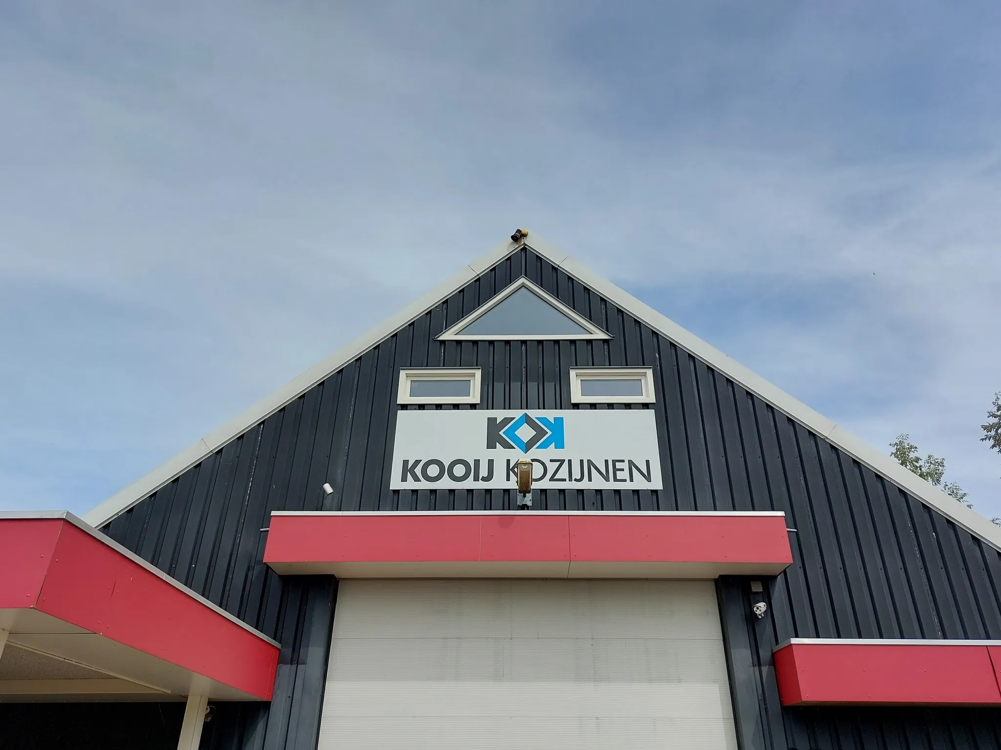 Vooraanzicht van het bedrijfspand van Kooij Kozijnen met een antracietgrijze gevel, rode accenten en diverse witte kunststof kozijnen nabij Leeuwarden.